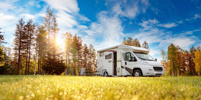RV parked in the grass on a sunny day with tall forest trees in the background. All Transmissions and Clutch provides exceptional RV transmission repair services in Vancouver WA and Camas WA.